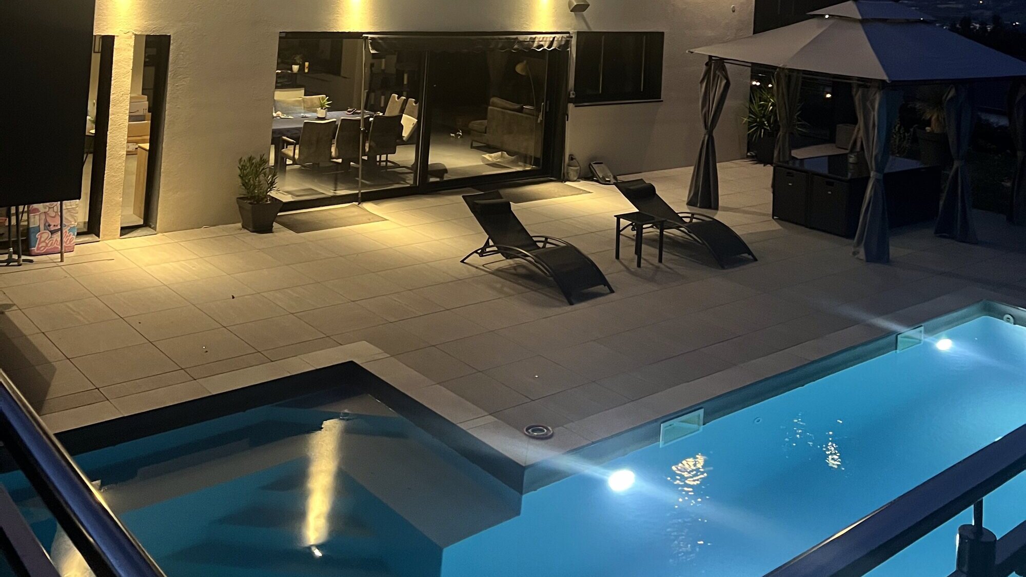 La piscine chauffée illuminée et la terrasse de la villa à la tombée de la nuit, en Haute-Savoie